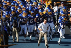 SJSU football team running out on to field behind coach. The team is suited up in their uniforms. 