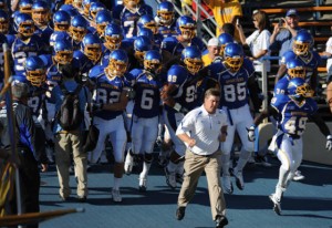 SJSU football team in uniform running out to the field with coach leading the way. 