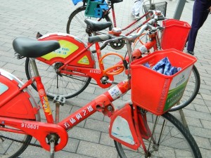 A picture of a red bike share bicycle taken in China during a Global Technology Initiative trip. Bikes include a modular shape and contains a basket for carrying items.