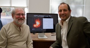 Two researchers studying the chemistry of interstellar cloud formation sit in front of a computer screen that has a picture of the emission research