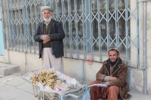 two men in traditional clothing with a wheelbarrow full of bananas