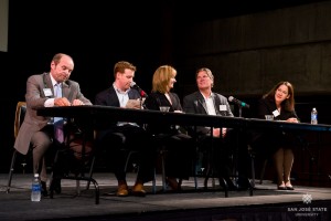 A discussion panel of industry professionals are sitting in chairs at a table on a stage