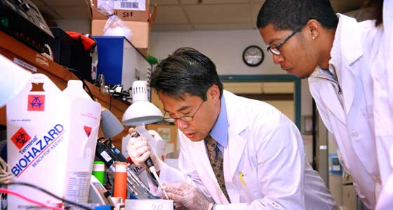 Male professor and male student (wearing white lab coats) in labratory carrying out tests using syringe.