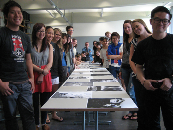 Graphic design students line up on both sides of a long table and pose for photo.