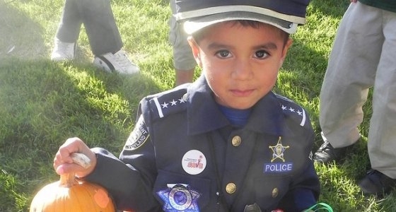 Little boy dressed in a police officer costume holding a tiny pumpkin.