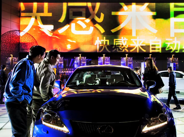 Image from essay showing everyday people examining a fancy sports car.