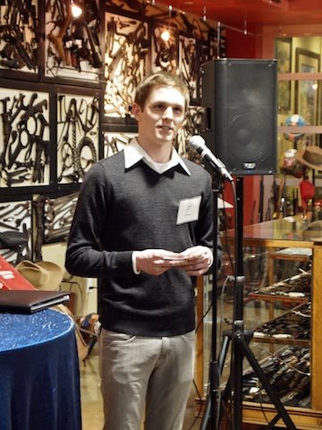 Business student wearing grey sweater giving speech in front of a mic