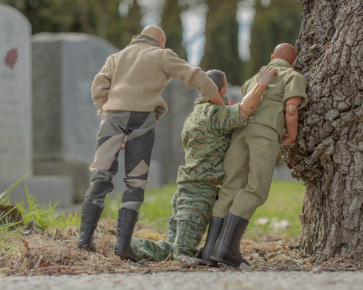 Soldiers, represented by action figures, mourn the loss of a comrade, with gravestones in the background.