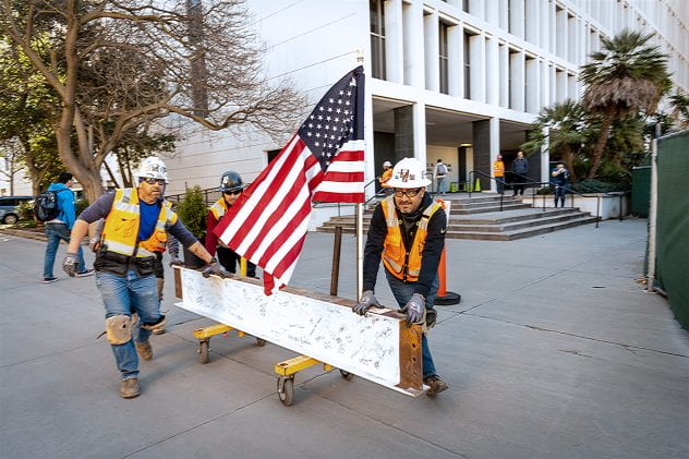 Two construction workers moving the signed ISB beam.