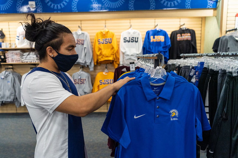 Student wearing a mask in the Spartan Bookstore looking through apparel.