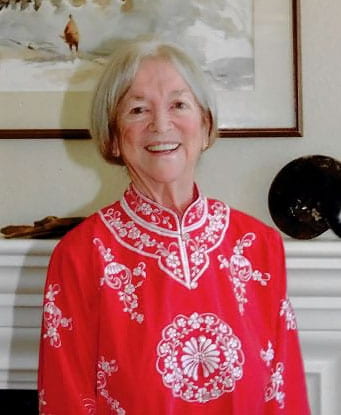 Sue Howland smiling in a bright read embroidered top.