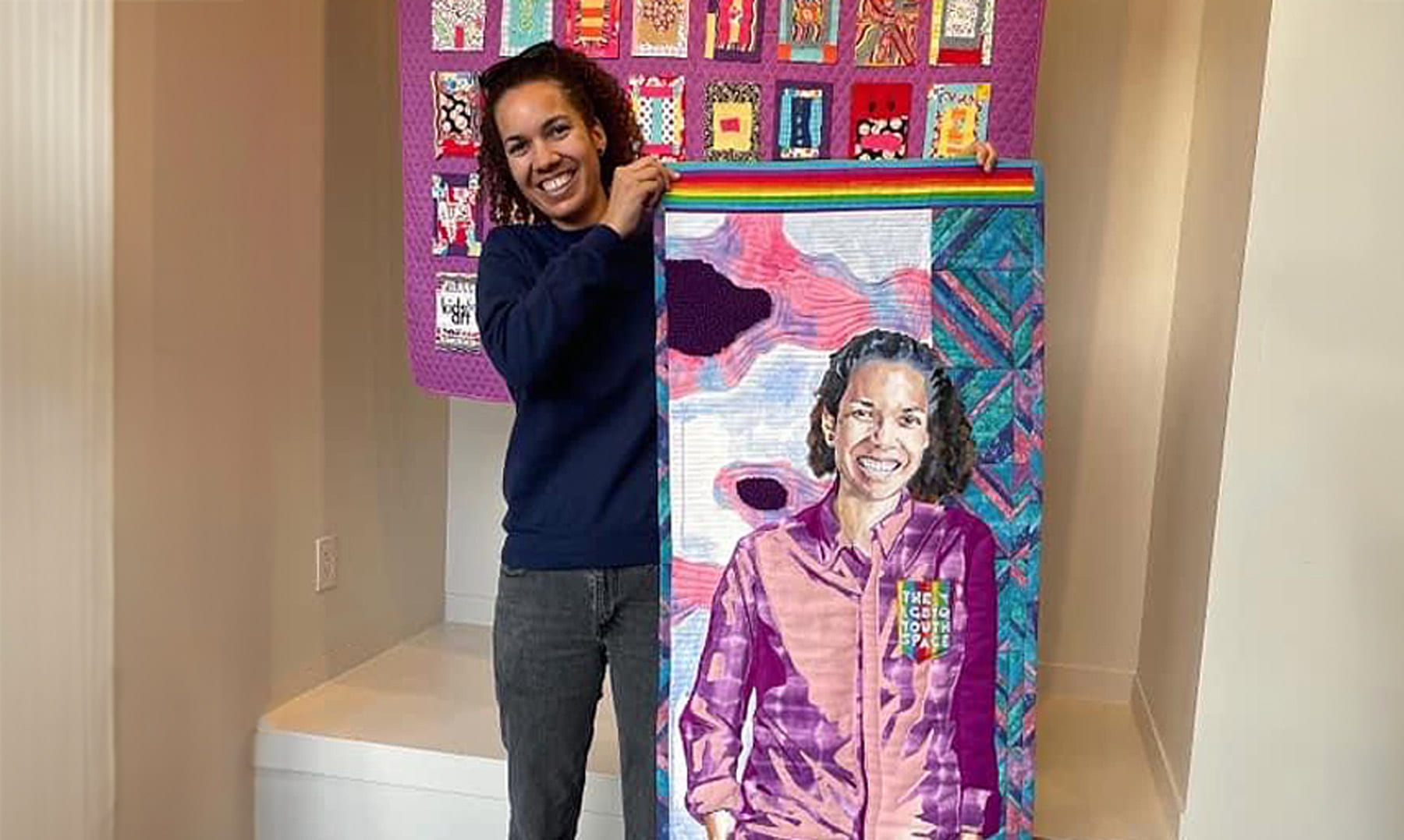 Alumna Adrienne Keel stands smiling with a self portrait made of fabric.